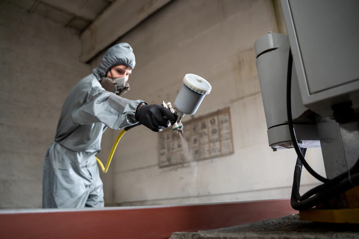 Profissional aplica tinta líquida com pistola pressurizada, utilizando técnica air spray em substrato metálico com preparação superficial controlada. 